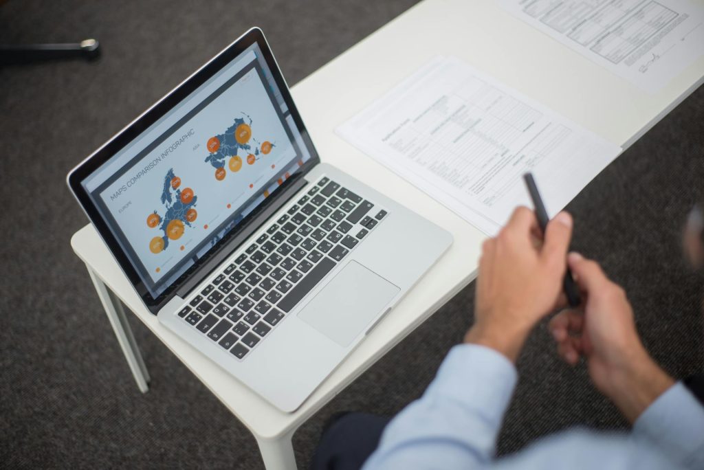 Business professional reviewing compliance and documentation materials with laptop and reports